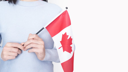 Unrecognized girl student in white blue shirt holding small Canadian flag over gray background, Canada day, holiday, vote, immigration, tax, copy space.の写真素材