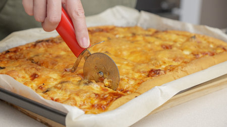 Cutting pizza with a round cutter knife. Close-up of delicious pizza being cut into pieces. Slow motion slicing a pizza into multiple slices with a cutterの写真素材