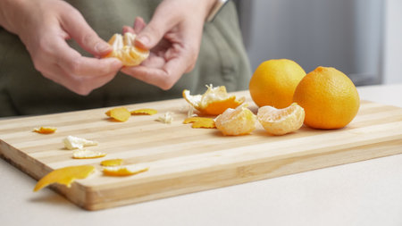 Hands peeling of orange tangerines on the cutting board on table, lots of juicy fresh fruits for cooking on Christmas.の写真素材