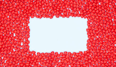This image features an abstract design of tiny red heart candies arranged to form a frame against a white background, creating a modern and visually appealing decorative element.の写真素材