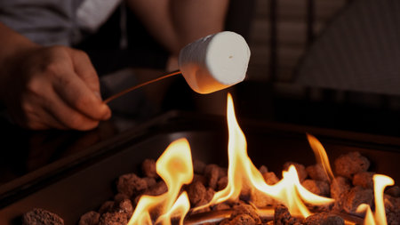 Close up of a marshmallow roasting over an open fire, creating a sweet treat. Enjoying warmth and flavors of summer with friends around the fire pit, making lasting memories.の写真素材