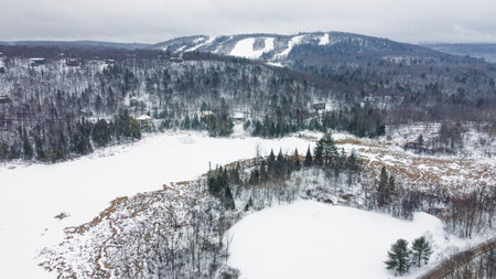 A serene winter landscape featuring a snow covered forest, ski slopes in the distance, and a frozen lake. Perfect for tourism promotions and showcasing winter beauty.の写真素材