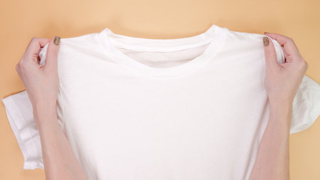 Close-up image of hands holding a white cotton t-shirt against a soft pastel background. Ideal for showcasing fashion, style, and casual wear concepts, with space for text.の写真素材