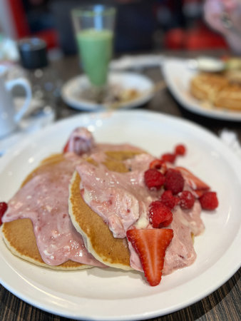 Enjoy a stack of pancakes topped with cream, strawberries, and raspberries. This delicious dish is perfect for breakfast or brunch, offering a sweet and fruity experience.の写真素材