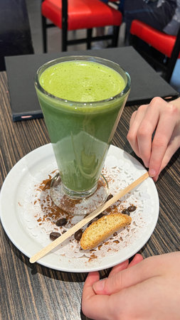 Savor a creamy matcha latte, elegantly garnished with a biscotti and coffee beans. This vibrant green drink is served on a fine plate, ideal for a cozy coffee shop experience.の写真素材