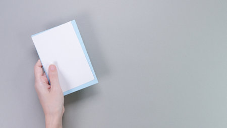 A hand is holding a blank white card with a light blue border, set against a soft gray background. This image is perfect for showcasing custom messages, creative designs, or mockup presentations.の写真素材