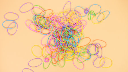 An overhead shot shows a colorful variety of rubber bands scattered on a soft peach background, ideal for crafting and creative projects, symbolizing flexibility and connection.の写真素材
