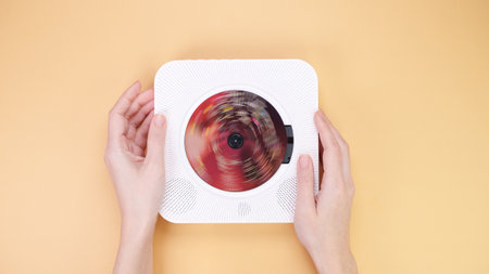 Overhead view of hands holding a sleek, white CD player with a disc spinning inside. Set against a solid pastel background, it showcases a modern aesthetic for music themes.の写真素材