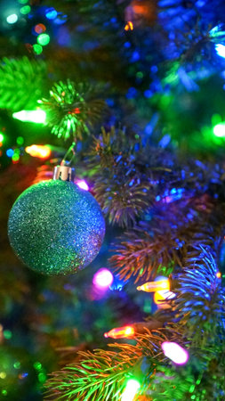 This image features a stunning Christmas tree adorned with green glitter balls and colorful lights against a dark background, perfect for holiday designs, cards, and festive projects.の写真素材