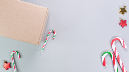 A vibrant festive flat lay featuring colorful candy canes, shiny star ornaments, and a cardboard box on a textured gray background. Perfect for holiday promotions and Christmas-themed designs.の写真素材