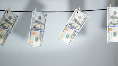 Hundred dollar bills are clipped to a clothesline, illustrating money laundering and illegal financial activities. Useful for finance and business articles or visuals.の写真素材