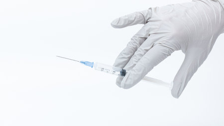 Healthcare worker in gloves is holding a syringe against a clean background, representing medical practices, vaccination, and health awarenessの写真素材