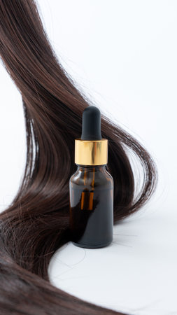Hair treatment serum bottle with a dropper is positioned next to smooth, shiny hair strands on a pristine white background, emphasizing hair careの写真素材