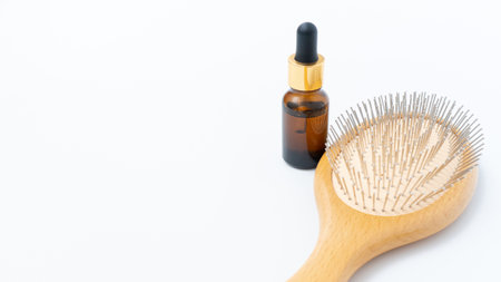 Hair loss treatment products featuring a wooden hairbrush and serum bottle arranged on a clean white background with ample copy space for marketingの写真素材