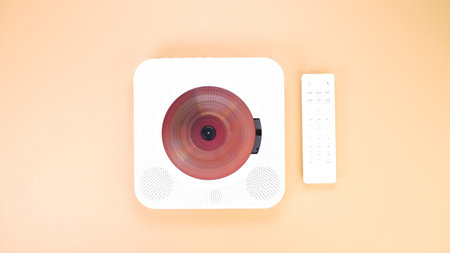 High-angle shot of a modern CD player with a remote control on a peach background. This stylish device combines retro charm with contemporary design, ideal for music lovers.の写真素材