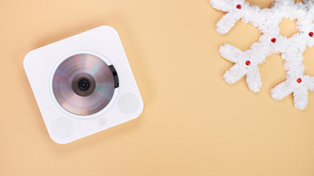A modern white CD player sits on a beige background next to a decorative white snowflake. Ideal for demonstrating sound technology and holiday spirit. Could be used for text placement mockup.の写真素材