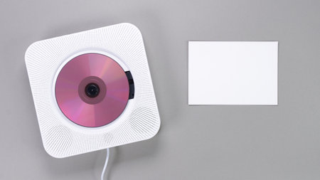 A chic pink wall-mounted CD player is elegantly displayed next to a blank white card on a solid gray background. Ideal for music concepts, promotions, or as a mockup for creative text and graphics.の写真素材