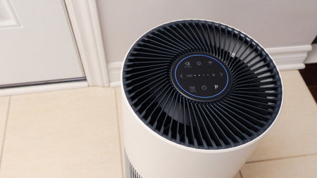 Tall round air purifier with a black top fan and a white body on a tile floor against the wall.の写真素材