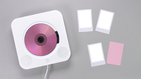 A sleek white CD player with a pink disc rests next to blank mockup photos on a grey background, symbolizing music and memories. Ideal for creative projects.の写真素材
