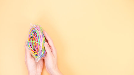 An overhead shot of hands holding a colorful bundle of rubber bands on a beige background. This...