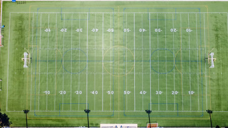 Aerial perspective of a pristine sports field featuring yard lines, goalposts, and lush green turf,...