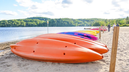 Colorful kayaks rest on sandy beach beside calm lake, with vibrant hues and serene nature backdrop, creating a perfect scene for outdoor activitiesの写真素材