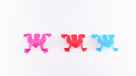 Three colorful plastic frogs in pink, red, and blue are arranged in a row on a bright white background, highlighting their playful design and charmの写真素材