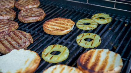 Grilled hamburger patties and pineapple slices are sizzling on barbecue grill, alongside toasted...