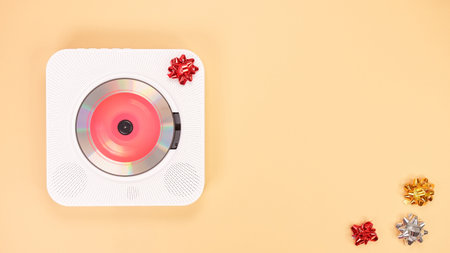 Overhead view of a sleek white CD player adorned with a red bow, ideal for gift presentations. Set against a peach background, it showcases a festive and modern music theme.の写真素材