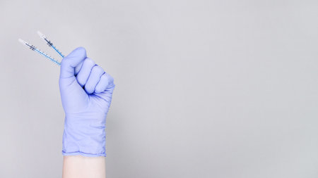 Gloved hand is raised, holding two syringes, representing flu shots, against a soft gray background, highlighting the importance of vaccination for healthの写真素材
