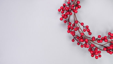A beautifully crafted red berry wreath is elegantly arranged on a soft gray background, enhancing the festive atmosphere ideal for Christmas celebrations and holiday decorationsの写真素材