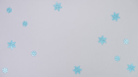 Scattered blue glitter snowflakes on a soft gray backdrop, evoking a whimsical winter scene filled with charm and a festive spiritの写真素材
