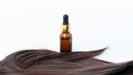 Hair treatment serum bottle positioned next to smooth hair strands on a bright white background, highlighting the importance of split ends care for beautiful hairの写真素材