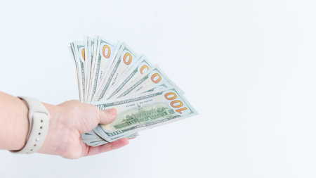 A hand showcases a fan of one hundred dollar bills against a clean white background. Represents...