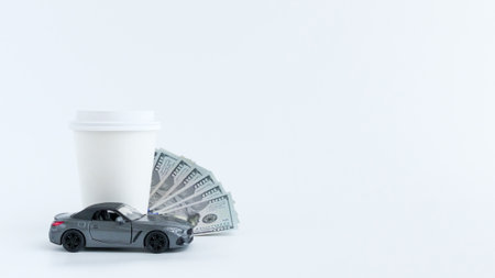 A toy car placed next to a coffee cup and a stack of cash, isolated on a clean white background, ideal for themes like financial freedom, luxury, and entrepreneurship.の写真素材