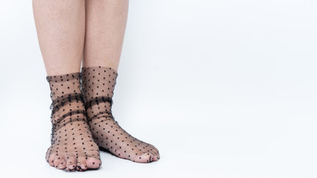 Female feet in sheer black polka dot socks, highlighting a trendy fashion choice against a minimalistic white background with ample copy spaceの写真素材