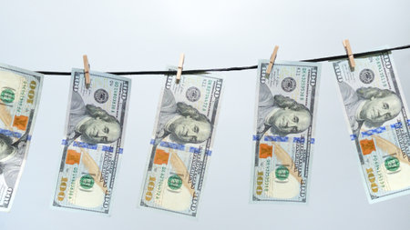 A symbolic image of money laundering, showcasing several one hundred dollar bills on a clothesline. This represents financial crime and the cleaning of dirty money for finance articles.の写真素材