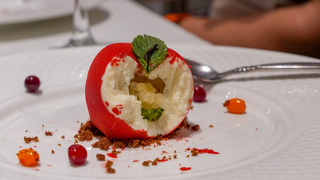 Unique red dessert resembling an apple, filled with creamy goodness and garnished with fresh mint,...