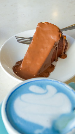 Blue matcha latte presented in a modern cup next to a rich chocolate dessert on a white plate, highlighting the vibrant colors and inviting textures of the sceneの写真素材