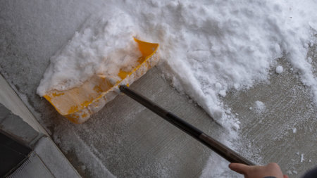 Snow shovel is actively removing fresh snow from a concrete walkway, highlighting winter weather...
