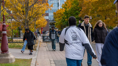 Ottawa ON, Canada - October 25, 2025: Woman in uOttawa jacket walks on campus during Open Doors event, with students and colorful autumn leaves creating a lively sceneのeditorial素材