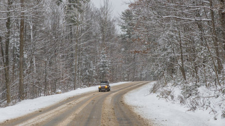 Gatineau QC, Canada - November 30, 2025: Winding road in a snowstorm with a car navigating through a winter forest, trees covered in snowのeditorial素材