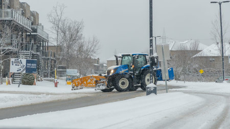 Gatineau QC, Canada - November 30, 2025: Blue tractor equipped with snow plow is clearing snow from...