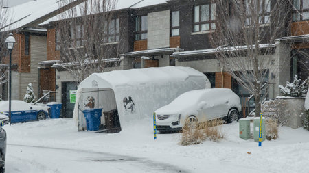 Gatineau QC, Canada - November 30, 2025: Snow blankets parked cars and a garage tent in a...