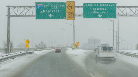 Gatineau QC, Canada - November 30, 2025: Snowstorm affecting highway with visible signs for Montreal and Gatineau, vehicles driving cautiously in winter conditionsのeditorial素材