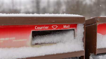 Gatineau QC, Canada - November 30, 2025: Snowy mailboxes with red and brown colors are partially...