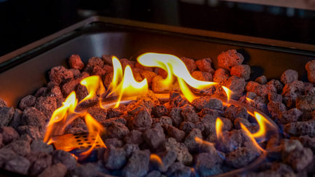 Flames flicker above volcanic rock in a fire pit, highlighting the vivid colors and textures of the...