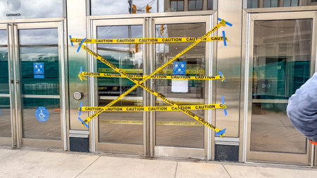 Ottawa ON, Canada - April 19, 2026: Caution tape is prominently displayed across the entrance doors of a building, with signs visible on the glass and reflections of the surrounding urban environment