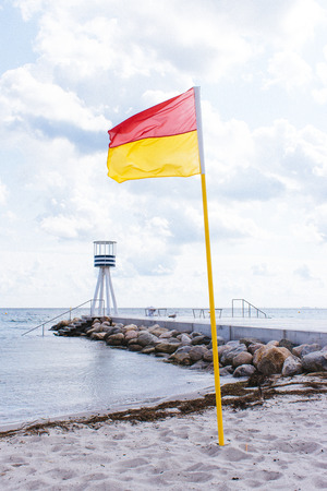Beautiful scenery of Klampenborgs (Denmark) base and lighthouse with sandy beach and rocks on a sunny day with some clouds on the seaside. Bathing flag in frontの写真素材