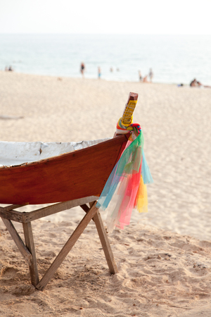 Red painted boat with colorful fabric at the peak standing at the beach of Koh Lanta, Thailand.の写真素材